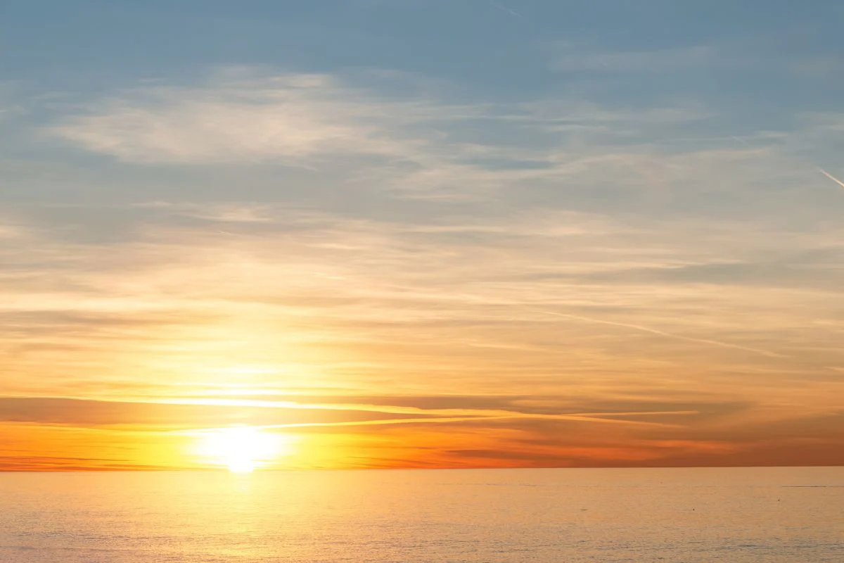 Sunset over calm ocean waters beneath a sky of orange and blue clouds.